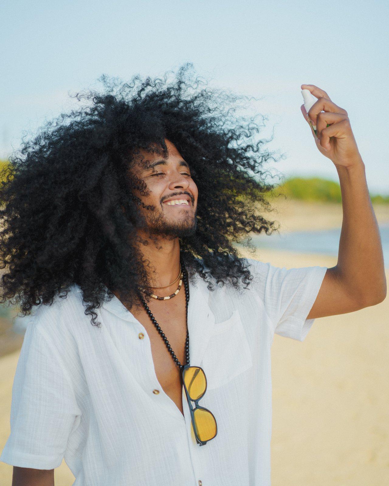 A model spraying a TRI·K hair product into his curls